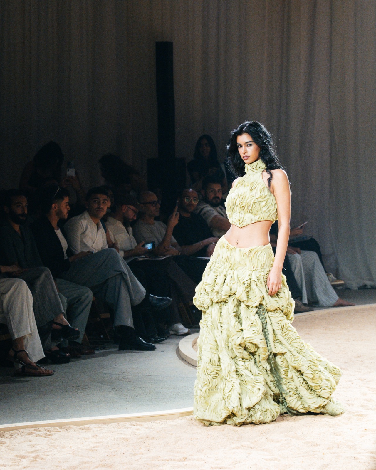 Pale-green couture gown on the sand-covered runway, front row watching